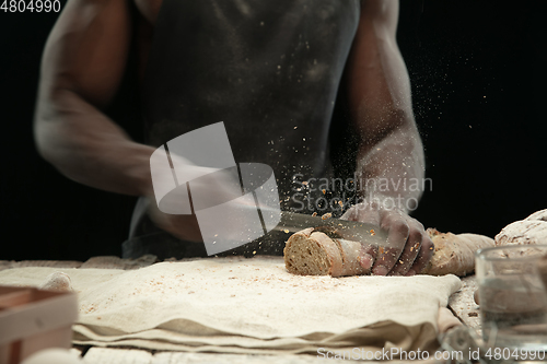Image of Close up of african-american man slices fresh bread with a kitchen knife