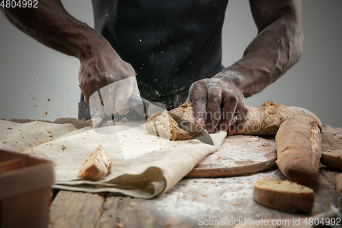 Image of Close up of african-american man slices fresh bread with a kitchen knife