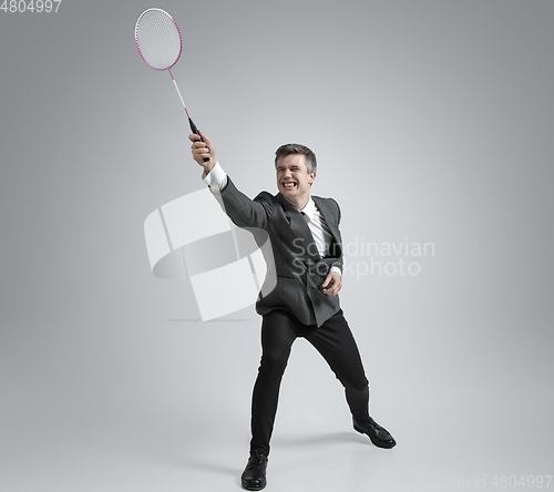 Image of Caucasian man in office clothes plays badminton isolated on grey studio background