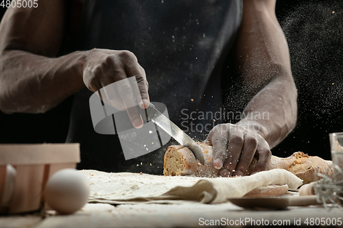 Image of Close up of african-american man slices fresh bread with a kitchen knife