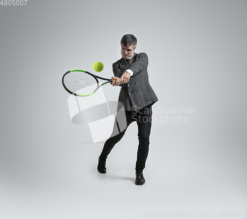 Image of Caucasian man in office clothes plays tennis isolated on grey studio background