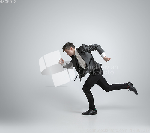 Image of Caucasian man in office clothes running isolated on grey studio background