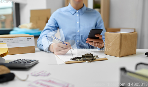 Image of woman with smartphone and clipboard at post office