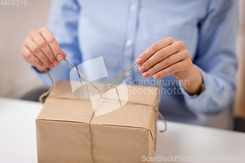 Image of woman packing parcel or gift box and tying rope