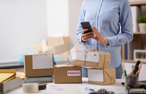 Image of woman with smartphone and parcels at post office