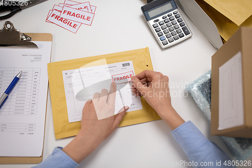 Image of hands sticking fragile marks to parcel in envelope