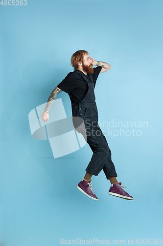 Image of Portrait of young caucasian man looks happy, jumping on blue background