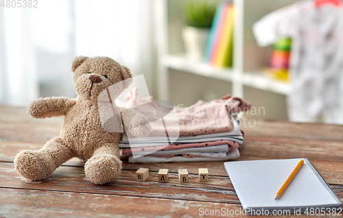 Image of baby clothes, teddy bear, toy blocks and notebook