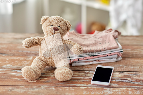 Image of baby clothes, teddy bear toy and smartphone