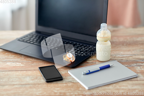 Image of baby milk formula, laptop and soother on table