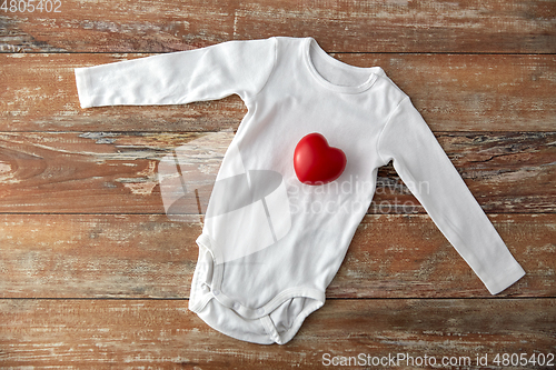 Image of baby bodysuit with red heart toy on wooden table