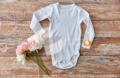 Image of baby bodysuit with soother and flowers on wood