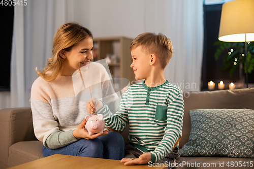 Image of mother and little son with piggy bank at home