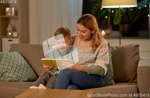 Image of happy mother and son reading book sofa at home