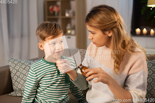Image of mother giving medication or cough syrup to ill son
