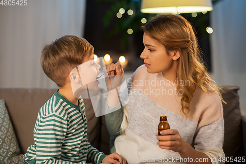 Image of mother giving medication or cough syrup to ill son