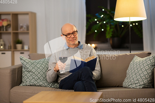 Image of happy senior man drinking wine and reading book