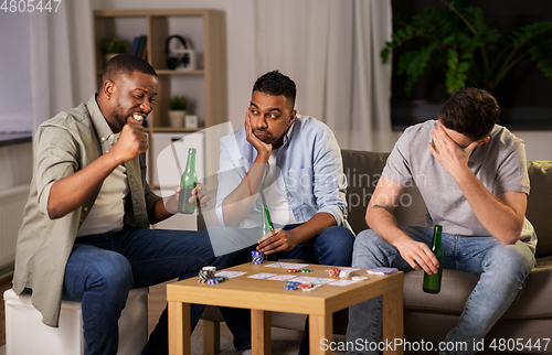 Image of male friends playing cards at home at night