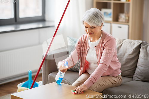 Image of senior woman with detergent cleaning table at home