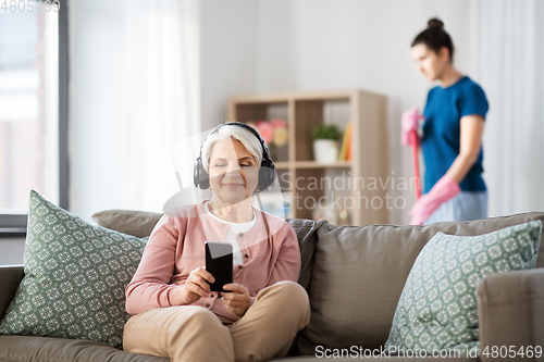 Image of old woman in headphones with smartphone at home