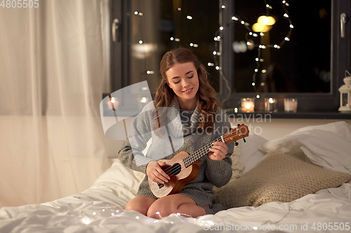 Image of happy young woman playing guitar in bed at home