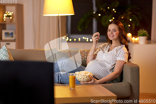 Image of pregnant woman with popcorn watching tv at home