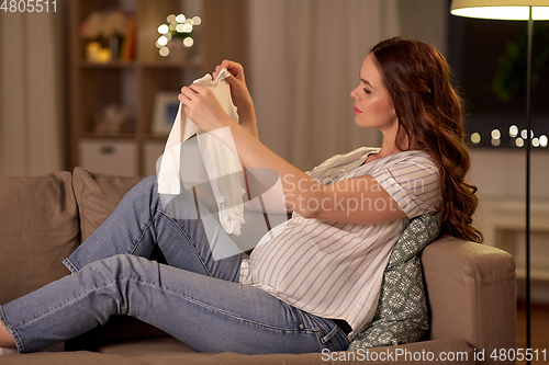 Image of happy pregnant woman with baby bodysuit at home