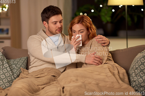 Image of sick young couple with tissue blowing nose at home