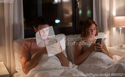 Image of couple using smartphones in bed at night at home