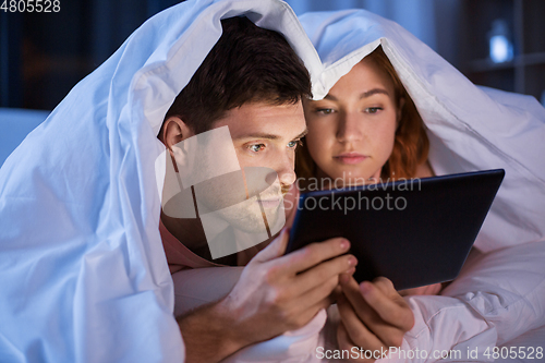 Image of couple using tablet pc in bed at night