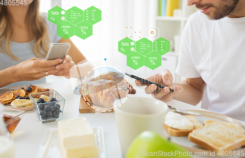 Image of couple with smartphones having breakfast at home