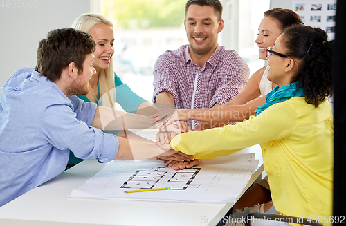 Image of happy architects with blueprint stacking hands