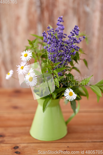 Image of bunch of herbs and flowers in green jug on table