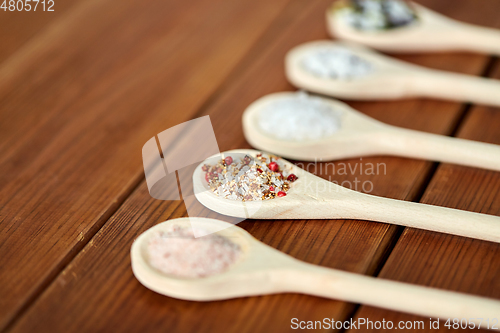 Image of spoons with salt and spices on wooden table