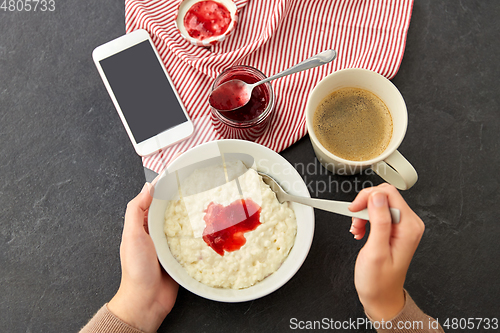 Image of hands with porridge, jam, spoon, coffee and phone