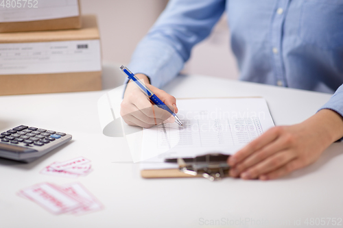 Image of woman with clipboard and parcels at post office