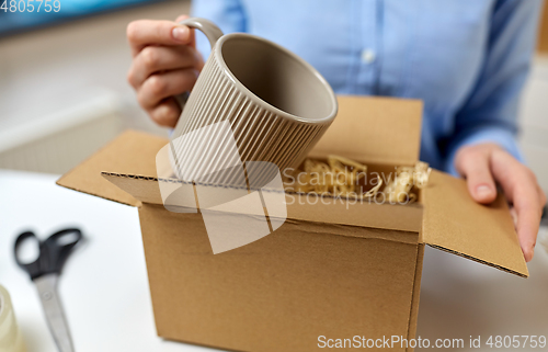 Image of woman packing mug to parcel box at post office