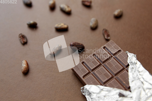 Image of dark chocolate bar in foil wrapper and cocoa beans