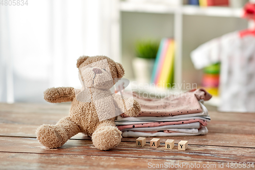 Image of baby clothes and teddy bear toy on table at home