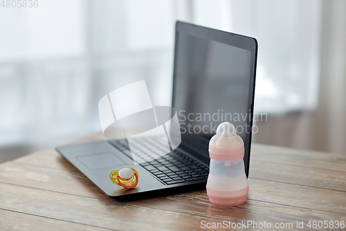 Image of baby milk formula, laptop and soother on table