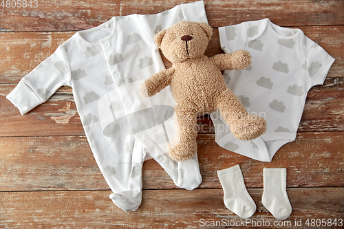 Image of baby bodysuits and teddy bear on wooden table