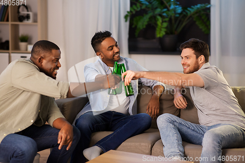 Image of happy male friends drinking beer at home at night