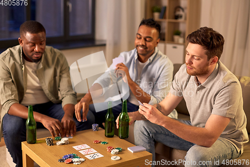 Image of smiling male friends playing cards at home