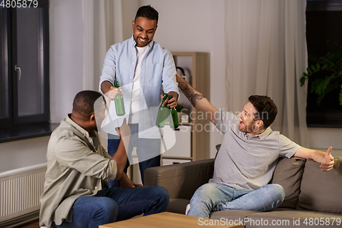 Image of happy male friends drinking beer at home at night