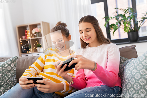 Image of happy teenage girls with smartphones at home