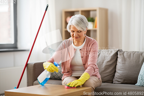 Image of senior woman with detergent cleaning table at home
