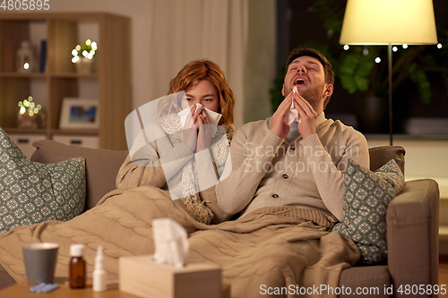 Image of sick young couple with tissue blowing nose at home