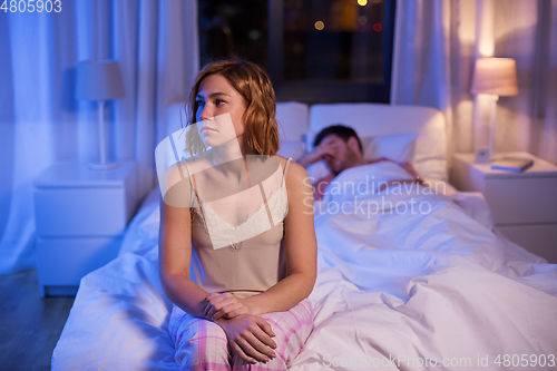 Image of sad woman with insomnia sitting on bed at night