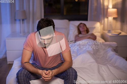 Image of sad man with insomnia sitting on bed at night