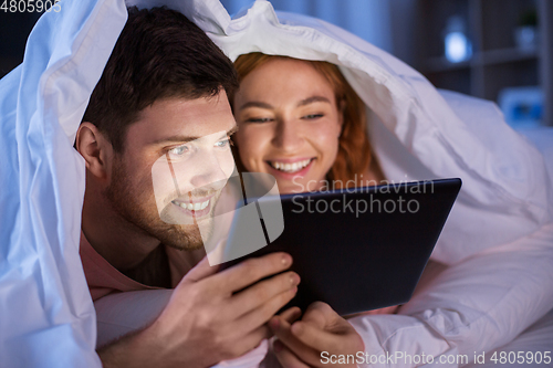Image of happy couple using tablet pc in bed at night
